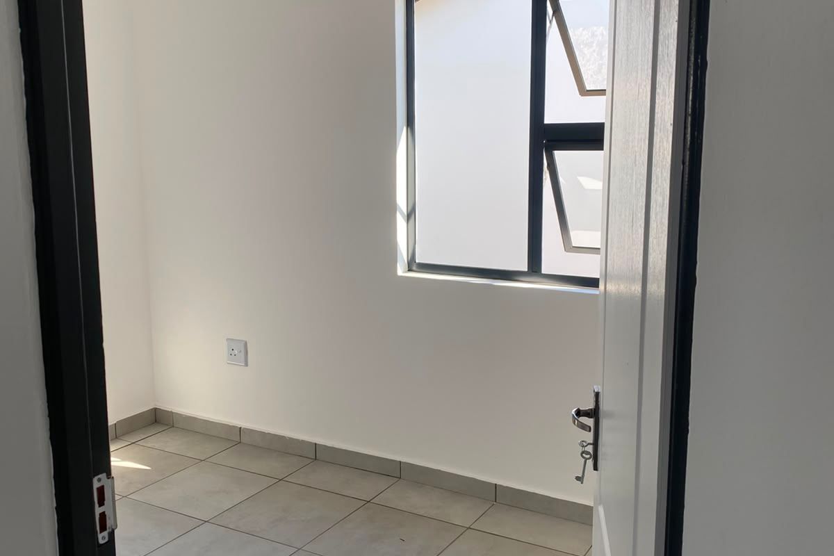 A clean, empty bedroom featuring neutral tiled flooring, white walls, and an aluminium window frame, ready for personalization.