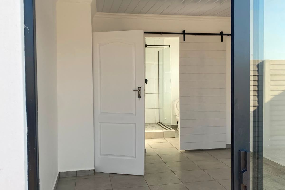 A bright, empty bedroom featuring tiled flooring, a tongue and groove ceiling, and a sliding barn door leading to an en-suite bathroom.