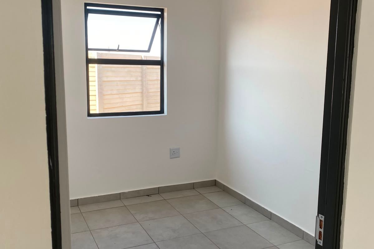 A clean, empty bedroom featuring neutral tiled flooring, white walls, and a top-hung window, providing a versatile space ready for personalization.