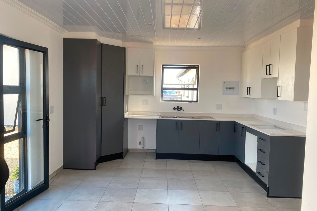 Modern kitchen featuring two-tone cabinetry, light tiled flooring, PVC ceiling, and direct access to the exterior through an aluminium framed door.