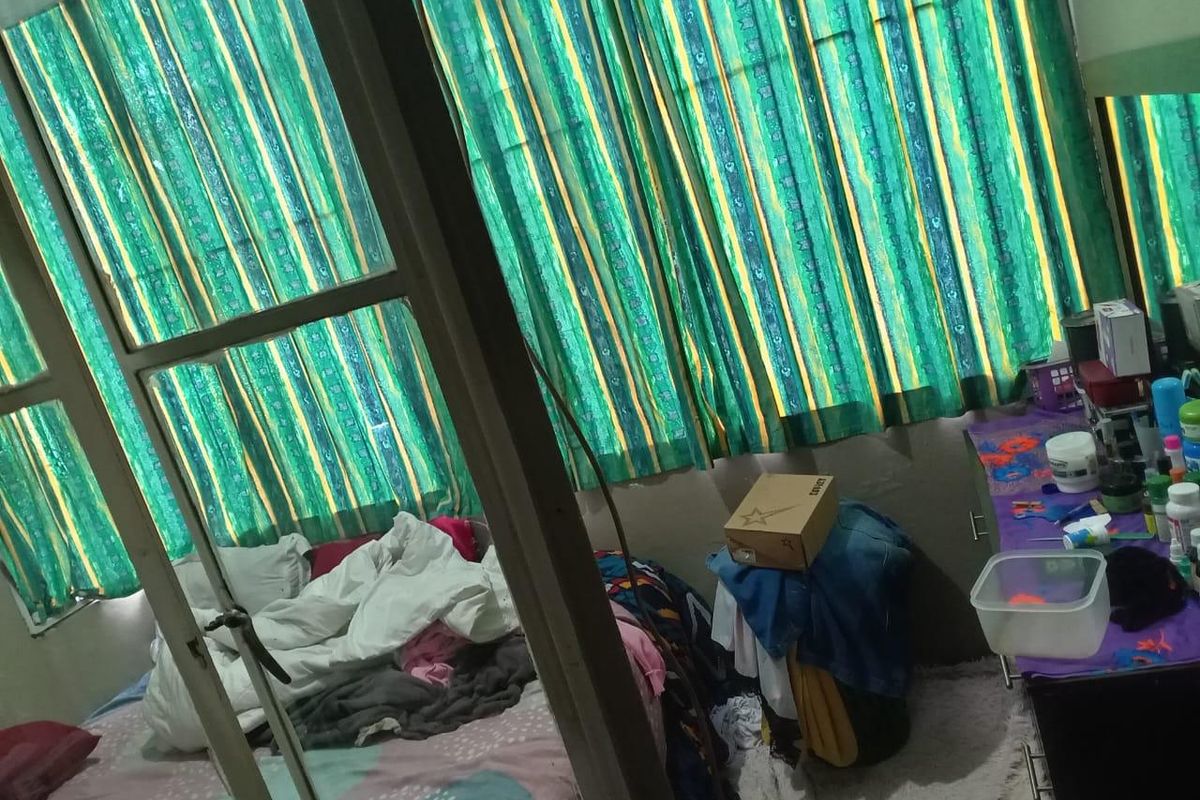 A bedroom featuring a window with patterned curtains and a built-in vanity area, requiring cosmetic updates to improve its overall appeal.