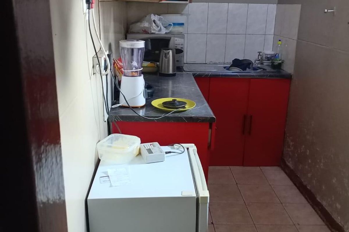 A compact kitchen featuring red cabinetry, laminate countertops, a stainless steel sink, and tiled flooring, requiring cosmetic updates to the wall finishes.