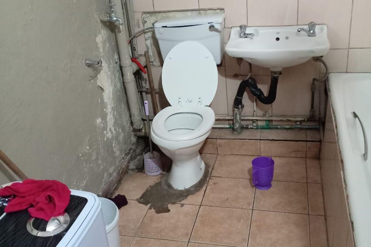 A bathroom requiring significant renovation, featuring a standard toilet, pedestal basin, and bathtub with visible wear to wall finishes and exposed plumbing.