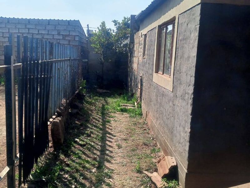 A narrow side or rear yard area featuring a metal fence, concrete block boundary wall, and exterior wall of the main dwelling.