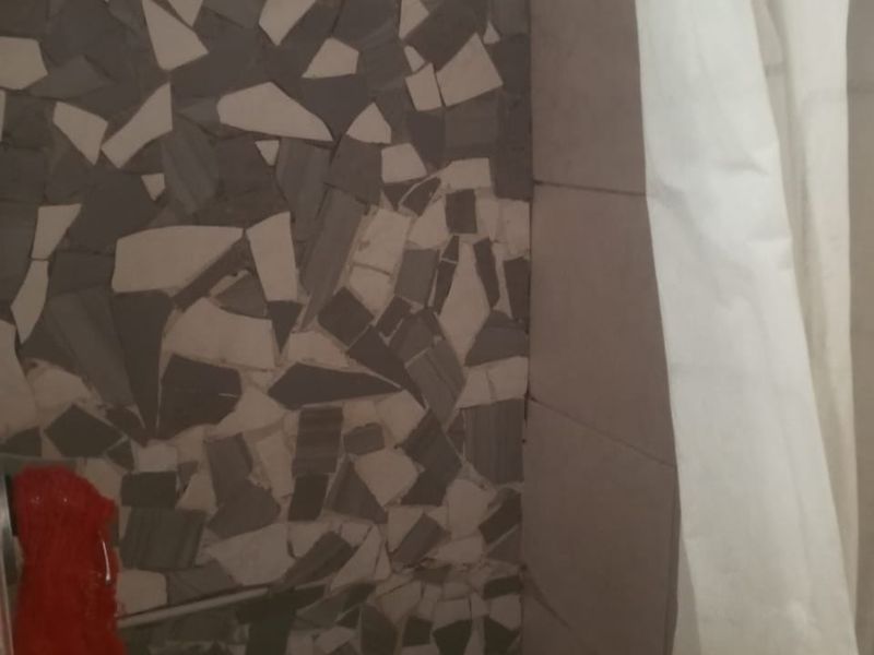 A shower area featuring a mosaic tile wall finish and a glass block window, currently showing signs of wear and dated tiling.
