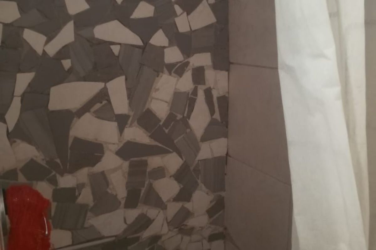 A shower area featuring a mosaic tile wall finish and a glass block window, currently showing signs of wear and dated tiling.