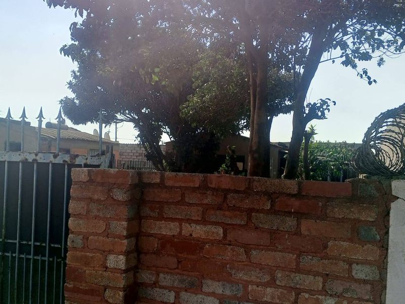 Front view of the property featuring a brick boundary wall, metal security gate, and perimeter razor wire.