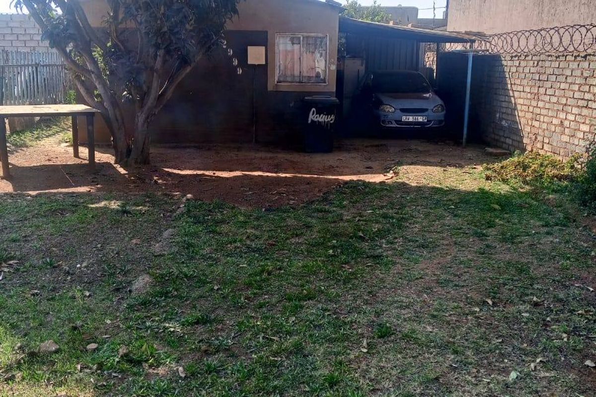 Rear exterior view of the property featuring a carport, brick boundary wall with security razor wire, and a grassed yard area.