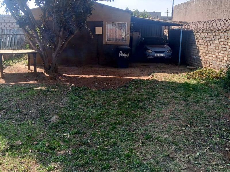 Rear exterior view of the property featuring a carport, brick boundary wall with security razor wire, and a grassed yard area.