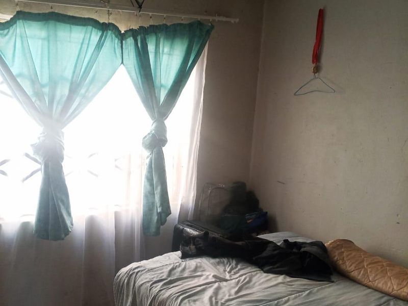 A bedroom featuring tiled flooring and a window with security bars, currently showing signs of significant wear and ceiling staining.