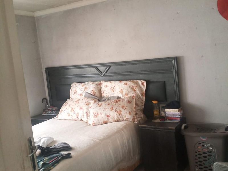 A bedroom featuring tiled flooring and a textured ceiling, currently requiring cosmetic updates to the wall finishes and general maintenance.