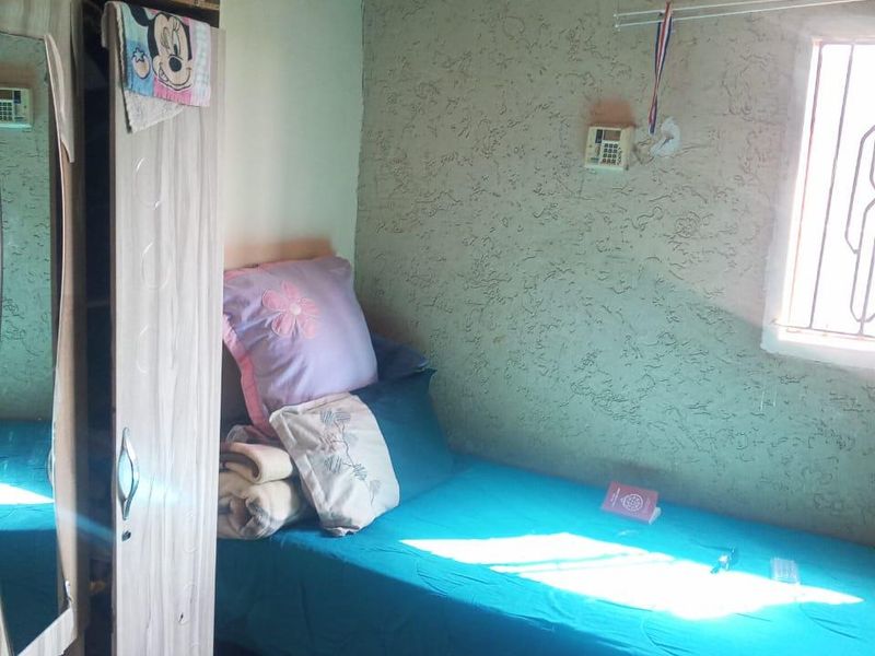 A compact bedroom featuring tiled flooring, textured walls, and a window fitted with security bars.