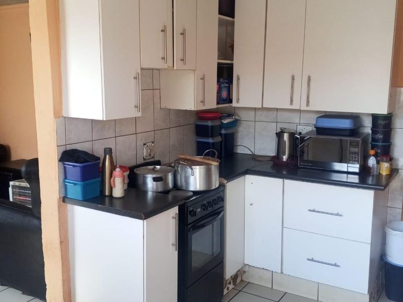 Compact kitchen featuring white cabinetry, dark countertops, and tiled flooring. The cabinetry shows significant signs of water damage and wear.