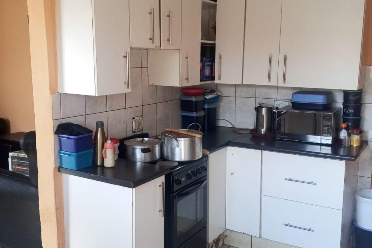 Compact kitchen featuring white cabinetry, dark countertops, and tiled flooring. The cabinetry shows significant signs of water damage and wear.