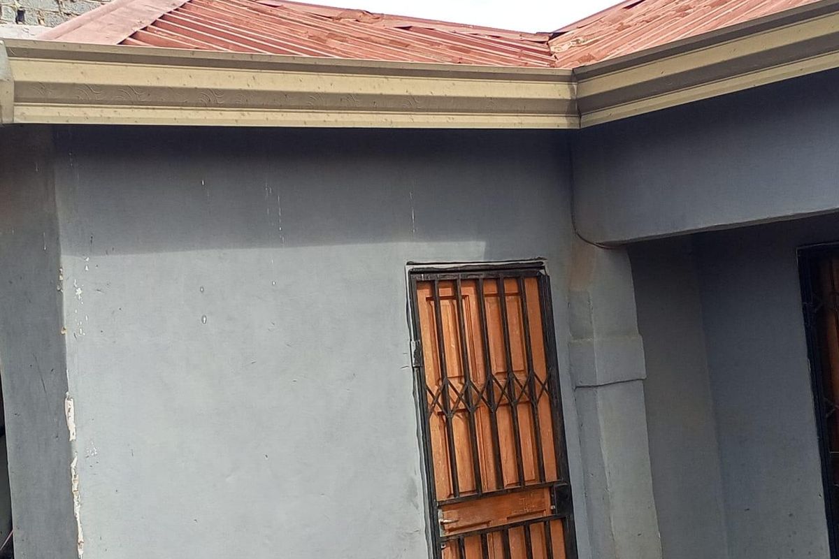 Exterior view of the property showing a corrugated metal roof with visible corrosion and a security gate entrance.