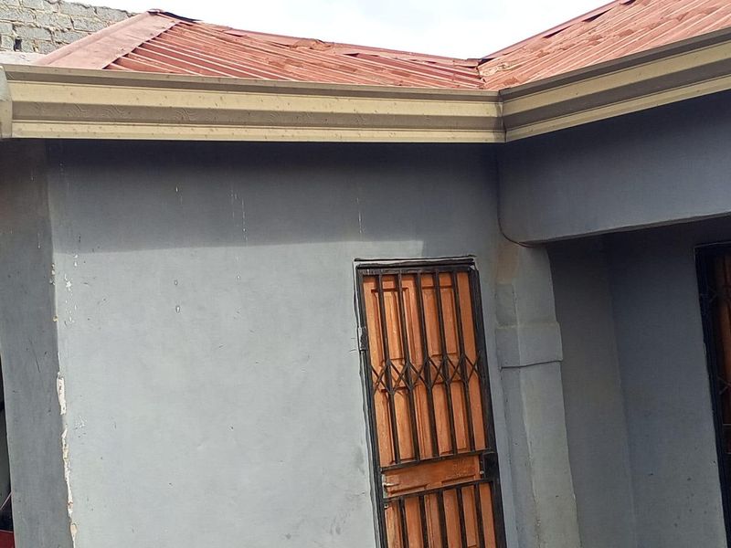 Exterior view of the property showing a corrugated metal roof with visible corrosion and a security gate entrance.