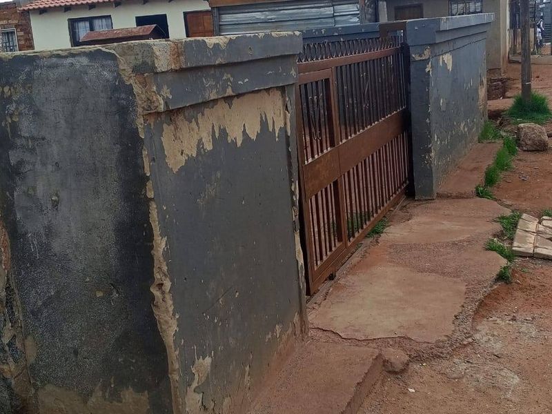 Front view of the property featuring a metal gate and a boundary wall with visible wear and peeling paint.