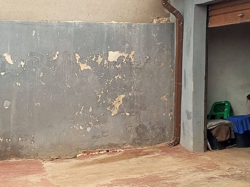A rear exterior area featuring a concrete paved surface and a boundary wall showing significant signs of weathering and paint deterioration.
