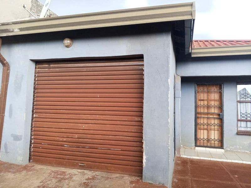 Front elevation of the property featuring a roller shutter garage door, a secure entrance with a metal gate, and paved exterior access.