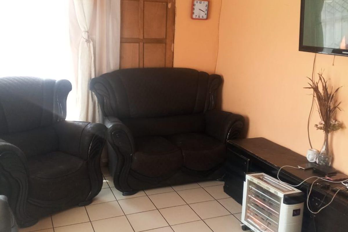 A living room featuring tiled flooring and a textured ceiling, currently showing signs of wear and dated finishes.