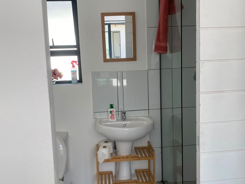 A functional bathroom featuring a pedestal basin, a glass-enclosed shower, and neutral floor tiling with a clean, modern aesthetic.