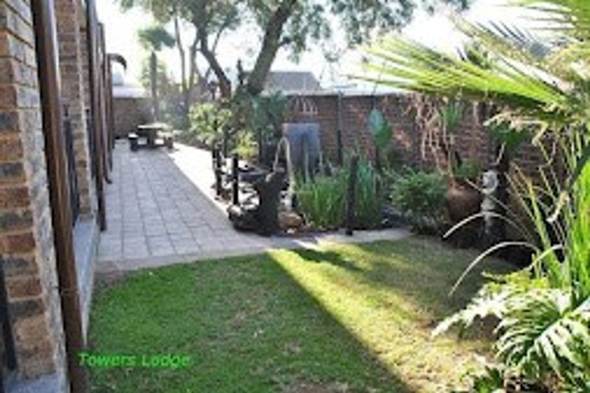 A rear garden area featuring a paved walkway, lawn, and brick boundary wall, providing outdoor space for the commercial property.