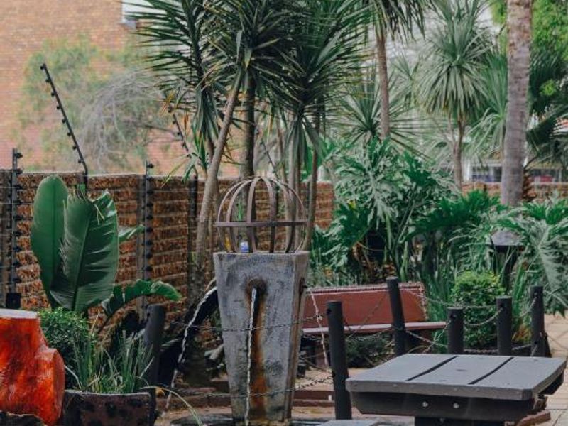 A paved outdoor patio area featuring a decorative water feature, established garden landscaping, and secure brick boundary walling with electric fencing.