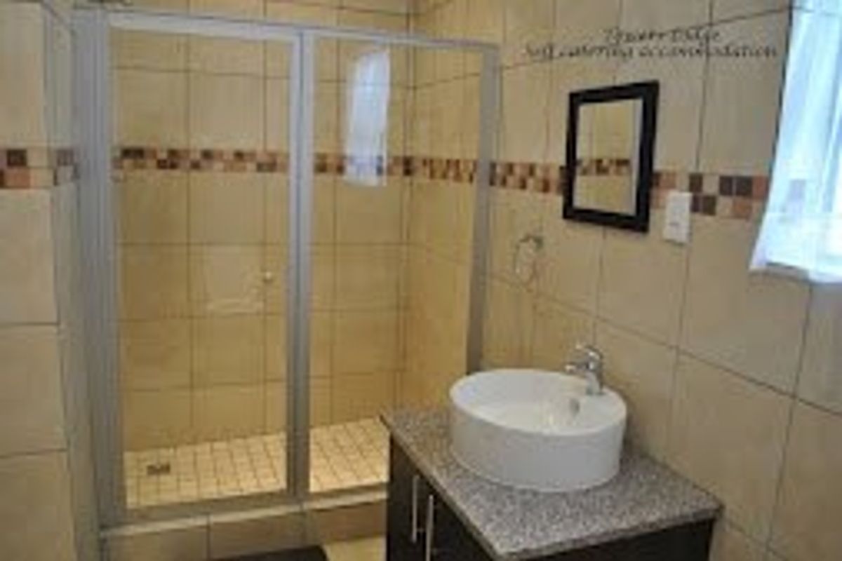 A functional bathroom featuring a glass shower enclosure, a modern vessel sink set on a vanity cabinet, and neutral wall tiling.