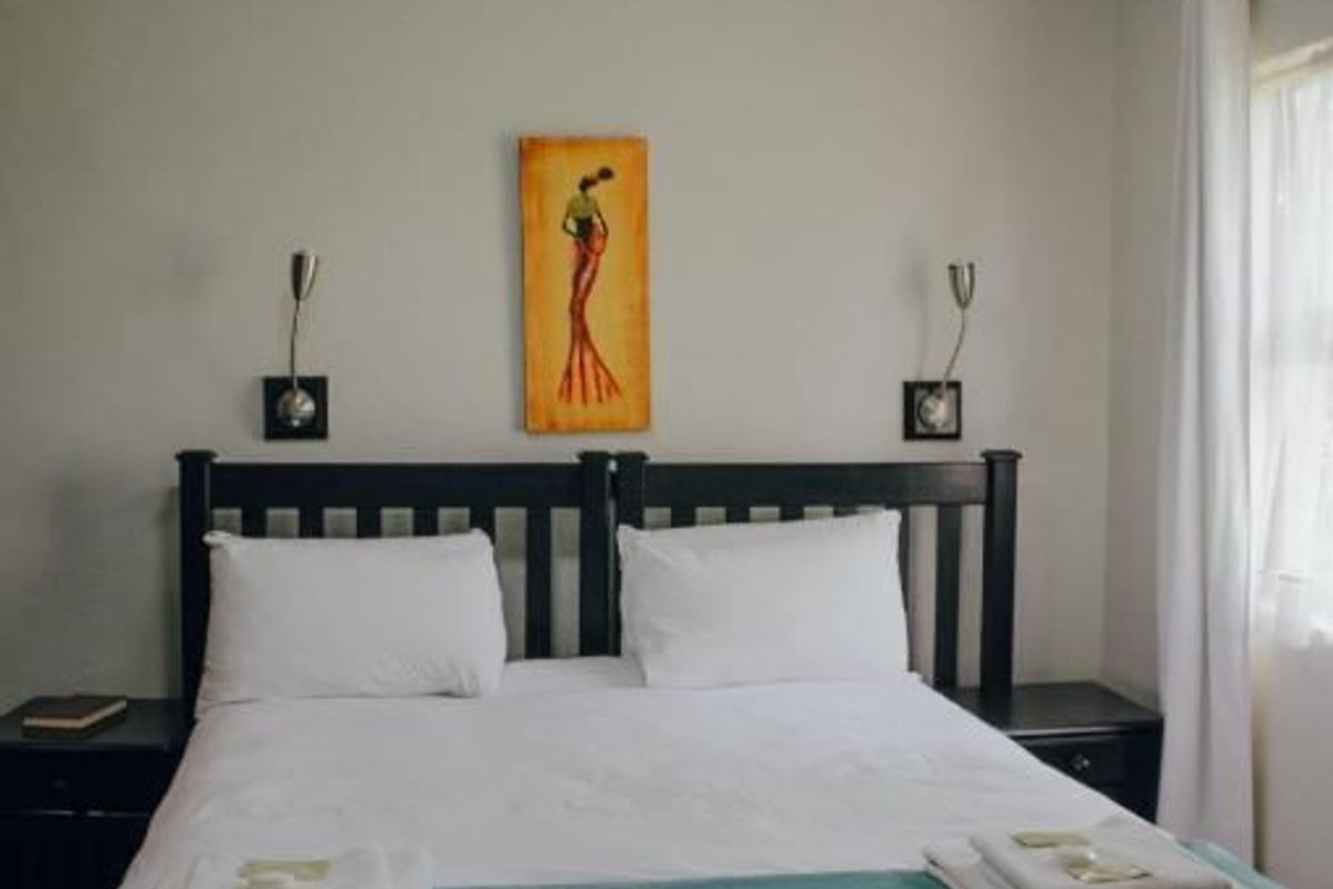 A well-maintained bedroom featuring neutral wall tones, modern wall-mounted reading lights, and a functional ceiling light fixture.