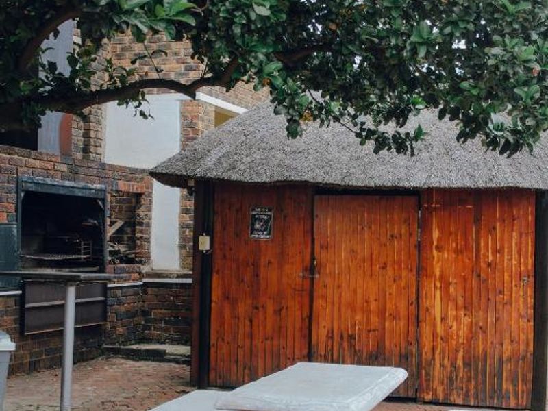 Outdoor entertainment area featuring a built-in brick braai, a thatched-roof structure, and paved flooring, providing a rustic space for social gatherings.