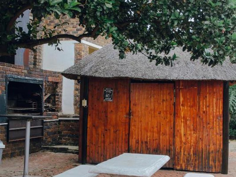 Outdoor entertainment area featuring a brick-paved patio, built-in braai, and a rustic thatch-roofed structure with timber paneling.