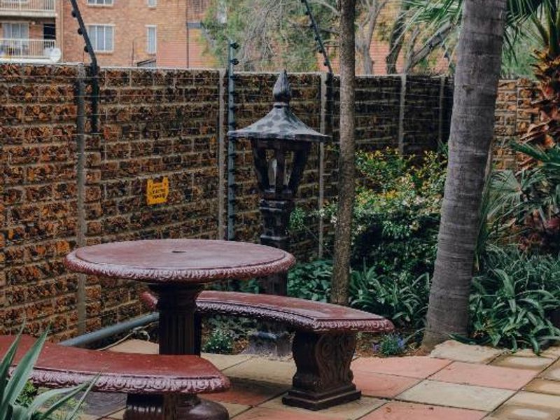 A paved outdoor patio area featuring a brick boundary wall with electric fencing and established garden landscaping.