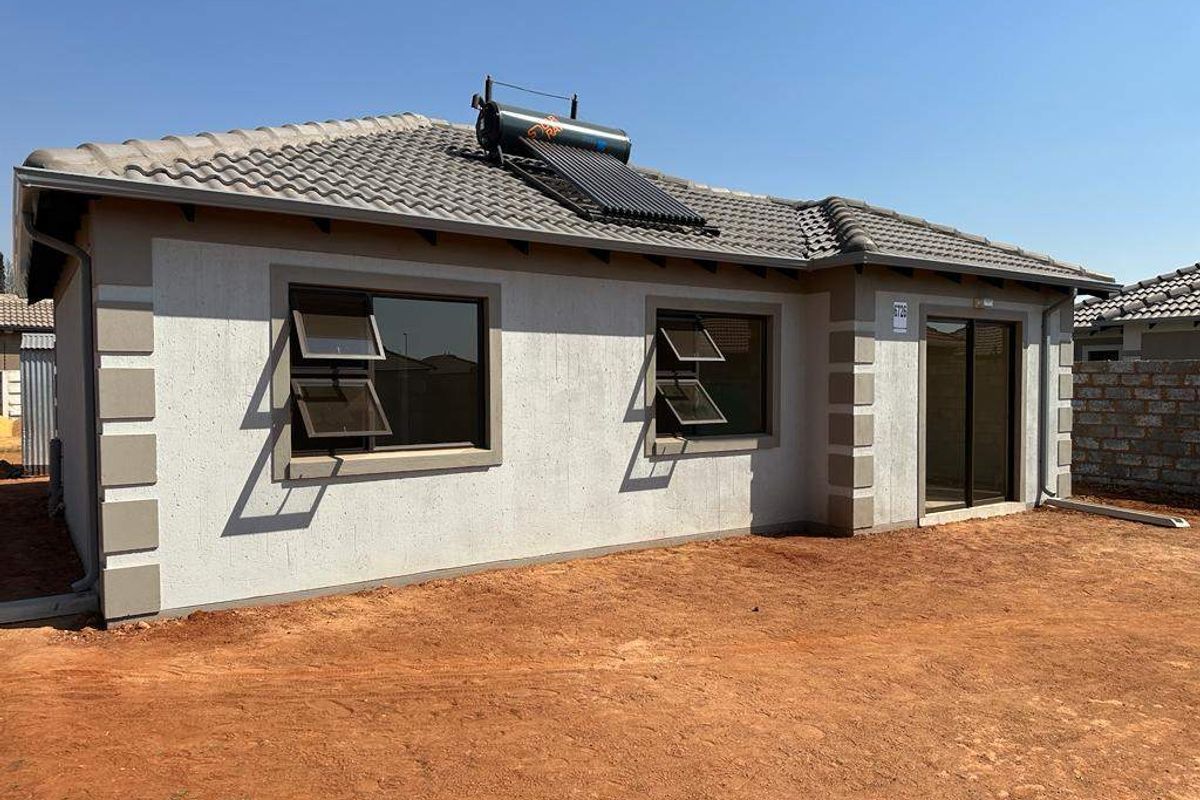 Rear view of a modern single-story house featuring a tiled roof, solar water heater, and aluminium window frames, set on an unlandscaped plot.