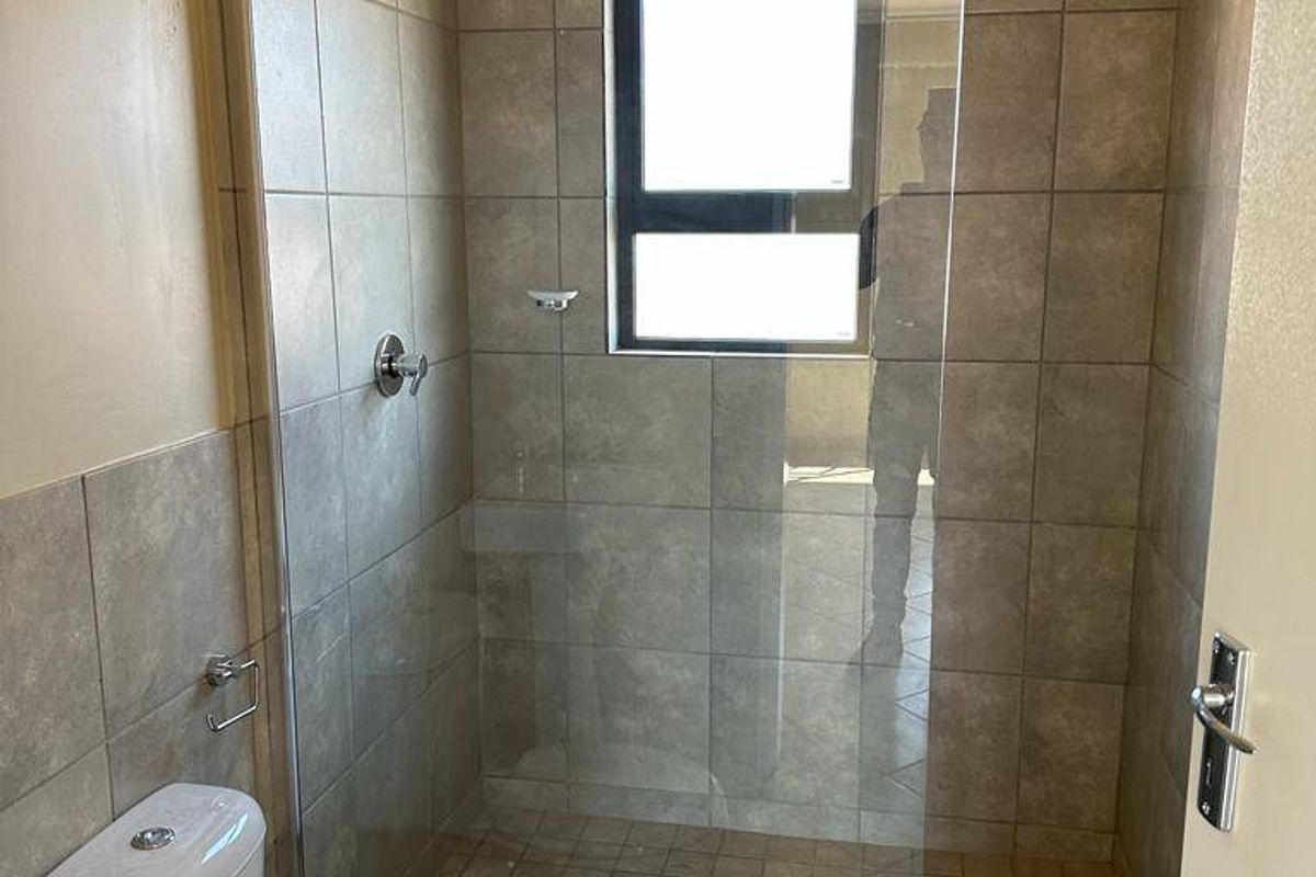 A clean, functional bathroom featuring a walk-in shower with a glass screen, tiled finishes, and a standard toilet.