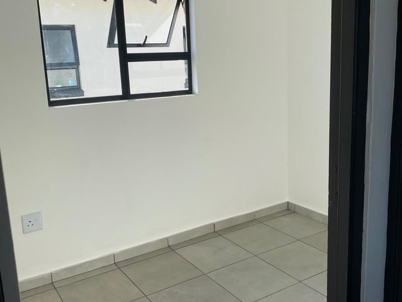 A clean, empty bedroom featuring neutral tiled flooring, white walls, and a modern aluminium-framed window, providing a versatile space ready for personalization.