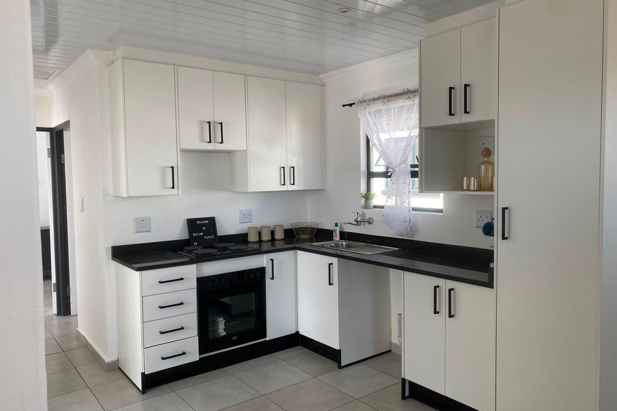 A clean, modern kitchen featuring white cabinetry, contrasting black countertops, built-in oven and hob, and neutral tiled flooring.