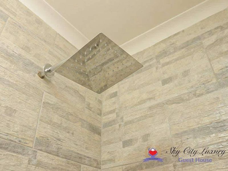 Close-up view of a modern square rainfall shower head mounted on stone-look tiled bathroom walls.