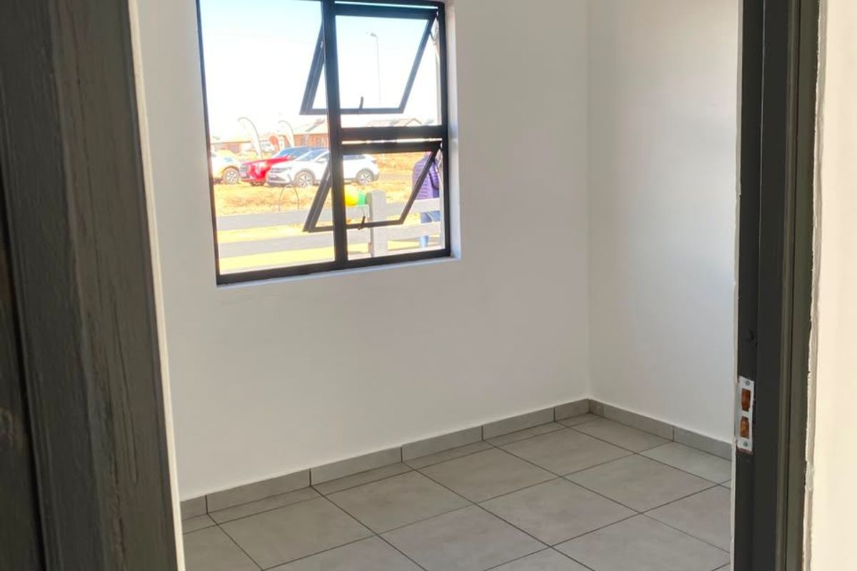 A clean, empty bedroom featuring neutral tiled flooring, white walls, and a modern aluminium window frame, ready for personalization.
