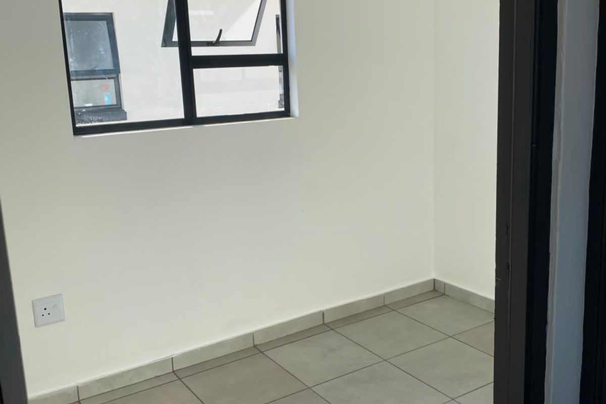 A clean, empty bedroom featuring neutral tiled flooring, white walls, and a modern aluminium-framed window.