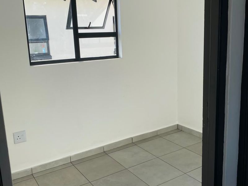 A clean, empty bedroom featuring neutral tiled flooring, white walls, and a modern aluminium-framed window.