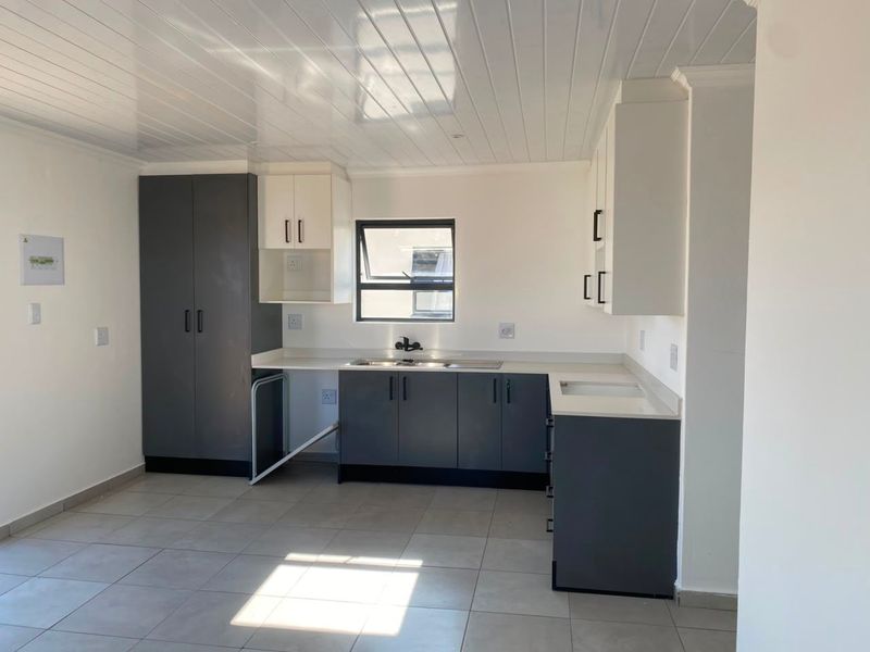 A modern, clean kitchen featuring two-tone cabinetry, stone countertops, a stainless steel sink, and tiled flooring under a white tongue and groove ceiling.