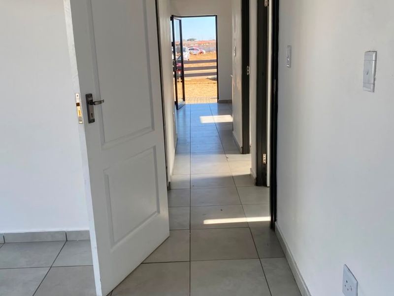 A clean, tiled hallway connecting interior spaces, featuring neutral white walls and direct access to the exterior.