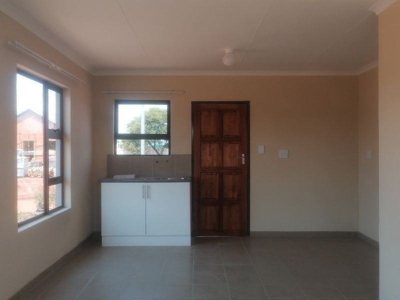 A compact, empty kitchen area featuring tiled flooring, a single sink cabinet with splashback, and a solid timber door.
