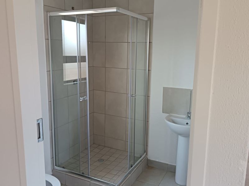 A functional bathroom featuring a corner shower enclosure with tiled walls and a pedestal basin, finished with neutral floor tiles.