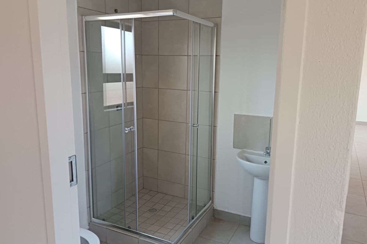 A functional bathroom featuring a corner shower enclosure with tiled walls and a pedestal basin, finished with neutral floor tiles.