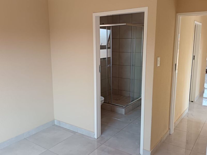 A clean, neutral-toned hallway featuring tiled flooring and direct access to an en-suite bathroom with a glass shower enclosure.
