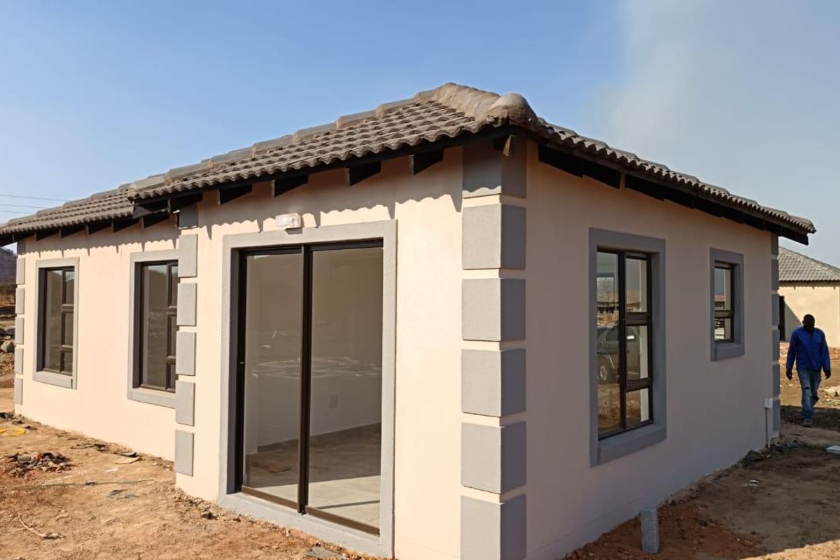 A modern single-story house exterior featuring a tiled roof, aluminium window frames, and a sliding glass door entrance, set in an developing residential area.