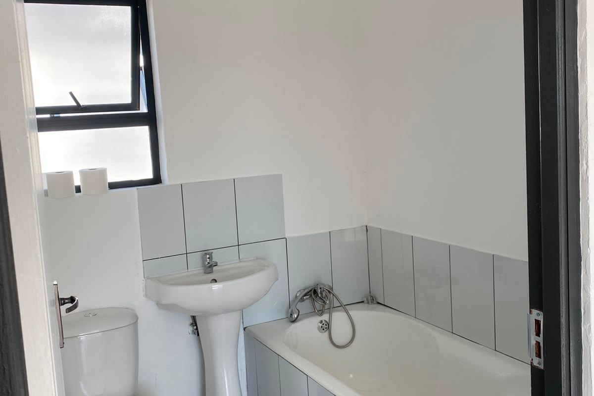 A functional bathroom featuring a pedestal basin, bathtub, toilet, and neutral tiled finishes, offering a clean and simple layout.