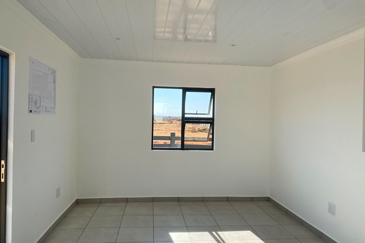 A bright, empty living area featuring neutral tiled flooring, clean white walls, and a modern tongue and groove ceiling with an aluminium window.
