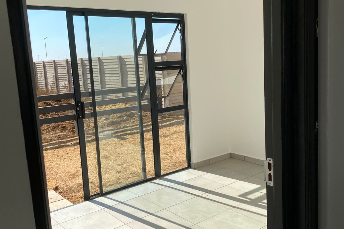 A bright, empty covered patio area featuring modern tiled flooring, a clean tongue and groove ceiling, and large sliding glass doors leading to the garden.